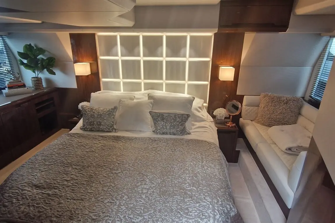 Luxurious bedroom featuring a bed with ornate cushions, a soft throw, a sleek sofa, and elegant lighting against a wooden backdrop.